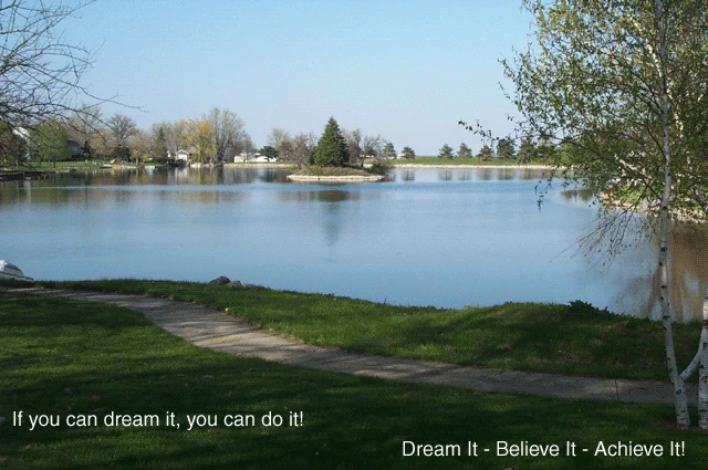 A spring photograph of the lake behind Herb Sieg's home, with the words 'If you can dream it, you can do it!' and 'Dream It — Believe It — Achieve It!' set over the grass and water.